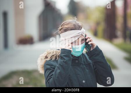 Flue and corona safety concept. Woman wearing face mask to protect herself and using smartphone. Outdoors Stock Photo