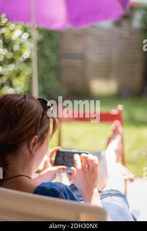 Lazy day at home. Sitting girl is enjoying the day on the porch, using her smartphone Stock Photo