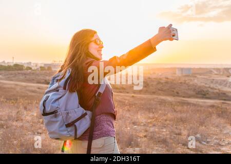 A young woman taking a selfie, while walking through the field at sunset. Stock Photo