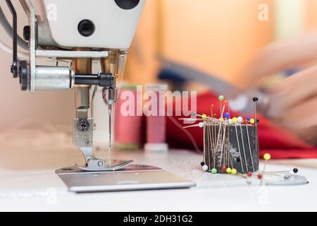 Sewing machine and needle in a dressmaker workshop: Close up tailor hands holding a needle Stock Photo
