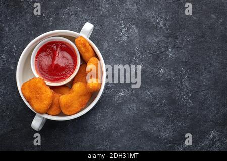Nuggets in a white deep plate, with sauce inside the plate, on dark concrete Stock Photo