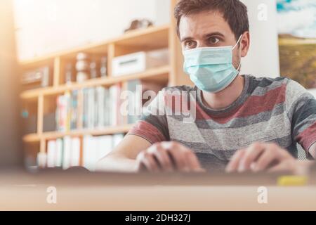 Protection in office during corona crisis: Man with face mask is sitting on his workplace. Stock Photo