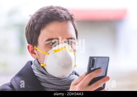 Flue and corona safety concept. Business man wearing face mask to protect himself and using smartphone. Outdoors Stock Photo