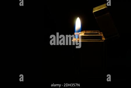 A flame against a dark background. An old and often used silver colored lighter glowing gold. Stock Photo