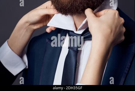 Womens hands tie around the neck of men classic suit model beard Stock Photo