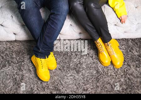 Demonstrating trendy colors 2021 - Gray and Yellow. Couple in similar clothes sitting on the sofa. Stock Photo