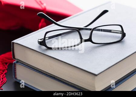 Books and glasses resting on a table with a cap in the background during a graduation celebration Stock Photo