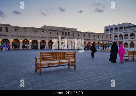 Souq Waqif in Doha Qatar main street at sunset with locals and visitors in the street , The old well fountain and pigeons flying Stock Photo