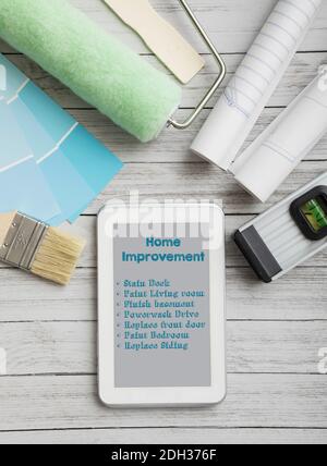 Home improvement checklist displayed on tablet with paint supplies and tools on wooden surface Stock Photo