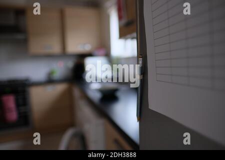 Pencil hanging on the front of the fridge, paper table stuck on the fridge door. Tracking groceries and writing down things that have to be purchased. Stock Photo