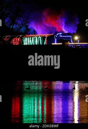 Illuminated Christmas steam train passes snowy railway station during ...