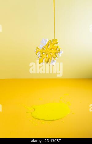 Bright yellow paint is pouring onto the snowflake hanging in the air. Puddle of paint under it. Creative background of the color of the year 2021 Stock Photo
