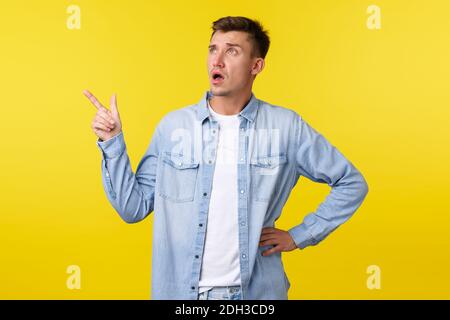 Confused and surprised startled handsome adult man asking question about product, looking and pointing finger upper left corner, Stock Photo