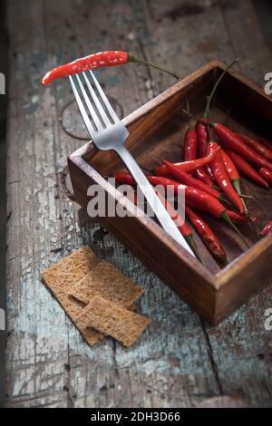 Hot chili peppers on a fork in a wooden mango tree box on a wooden bench. Copy space.Top view Stock Photo