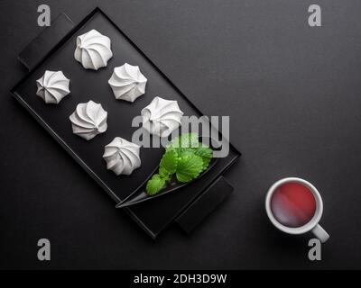 White meringue from egg white on black tray and cup of tea from fresh mint leaves. Overhead shot. Stock Photo