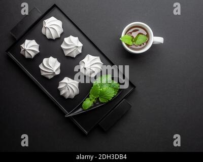 White meringue from egg white on black tray and cup of tea from fresh mint leaves. Overhead shot. Stock Photo
