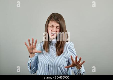 Claw hands, hand gesture and sign, scary desperate, showing claws, nails, making silly face. Young attractive woman, dressed blue shirt with brown eyes, brunette hair, grey background Stock Photo