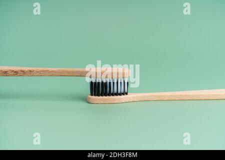Two Eco-friendly antibacterial bamboo wood toothbrushes with white and black bristles on a light green background. Taking care of the environment is t Stock Photo