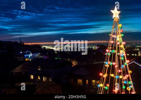 A colorful Christmas tree lawn decoration with a star on top with the evening skyline of a city and valley behind, in Spokane Washington USA Stock Photo