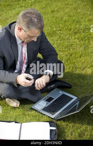 Geschäftsmann sitzt auf einer Wiese, schaut auf die Uhr, Laptop, Computer, MR:Yes