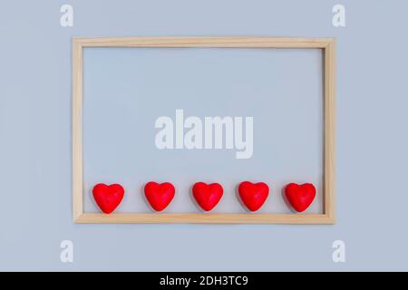 Valentines day and love concept: Rectangular wooden frame with red hearts inside on light blue background. Top view, close up, macro. Stock Photo
