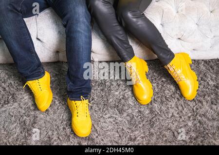 Demonstrating trendy colors 2021 - Gray and Yellow. Couple in similar clothes sitting on the sofa. Stock Photo