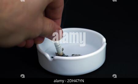 Put out a cigarette in an ashtray.Ashtray on a black background.Man puts out a cigarette, smoking. Stock Photo