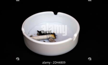 Ashtray with cigarette butts on a black background, white ashtray, close-up. Stock Photo