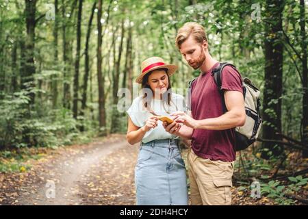Hikers using mobile gps for directions. Happy couple checking smartphone in the woods during backpacking trip. Young joyful coup Stock Photo