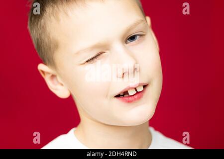 Winking teen boy 7-10 in white t-shirt on red background Stock Photo