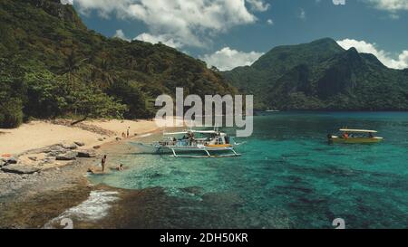 Passenger boat at ocean beach aerial view. People resting, swiming on sand at sea bay water. Amazing landscape of Philippines tropical nature with jungle forest and mountain. Cinematic paradise resort Stock Photo