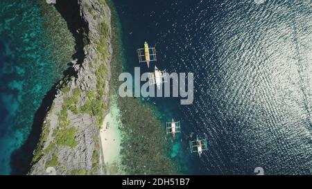 Passenger boats at shallow water of ocean bay top down aerial view. Cinematic summer vacation scenery of cruise on vessels at Philippines archipelago islands. Epic seascape with sun reflection