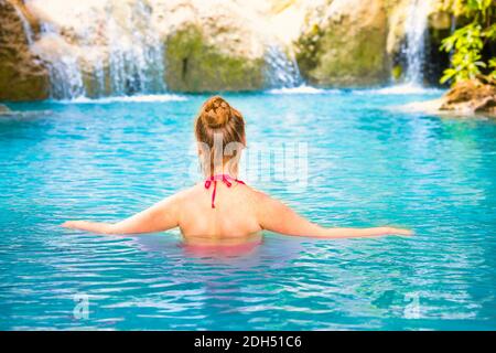 Rear view of young woman relaxes in emerald blue lake, Erawan National park, Thailand Stock Photo