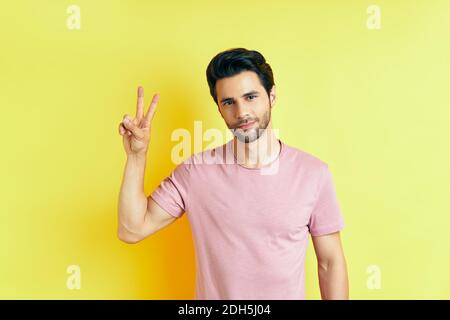 Young handsome man show victory sign on yellow background Stock Photo