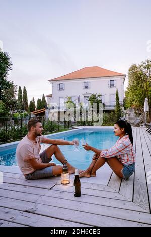 French vacation home with wooden deck and swimming pool in the Ardeche France. Couple relaxing by the pool with wooden deck duri