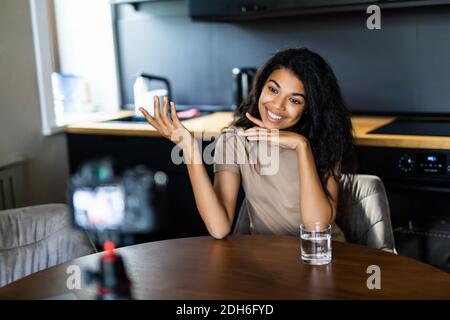 Beauty blogger woman filming routine tutorial near camera on tripod. Influencer mixed race woman live streaming product review in home studio Stock Photo