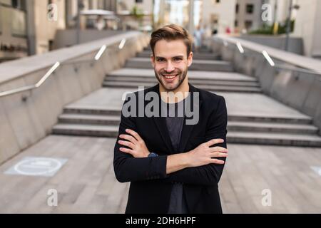 Caucasian male banker with crossed hands standing at urbanity in financial district and thoughtful looking away, Stock Photo