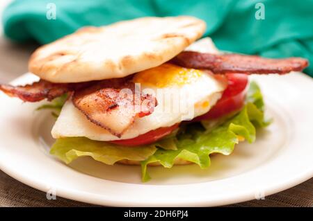 breakfast sandwich wiuth crispy bacon, farm fresh egg, tomato and lettuce on naan flatbread Stock Photo