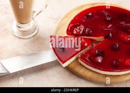 Homemade cherry and strawberry cheesecake, latte macchiato cup, cut piece of pie on knife Stock Photo
