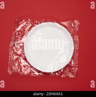 Disposable white plastic plates in transparent plastic packaging on a red background Stock Photo