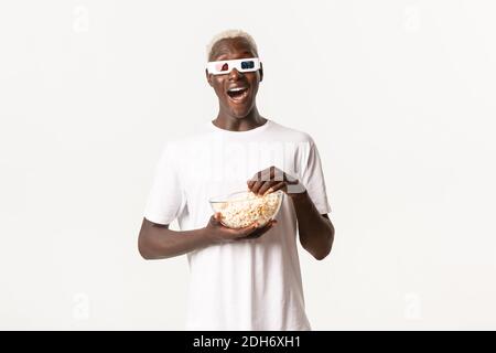 Portrait of amused carefree african-american guy, wearing 3d glasses and looking excited while watching movie, eating popcorn, s Stock Photo