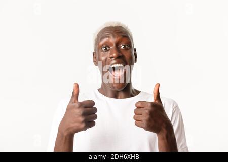 Portrait of cheerful and excited handsome african-american blond guy looking with rejoice, showing thumbs-up and smiling, approv Stock Photo