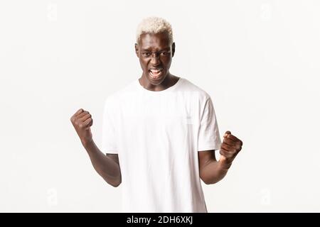Portrait of confident and strong african-american blond man, clenching fists and shouting encouraged, standing white background Stock Photo
