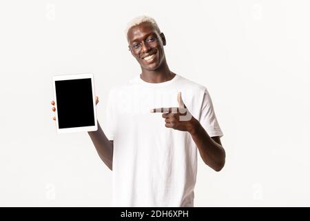 Portrait of attractive smiling african-american guy in glasses pointing finger at digital tablet screen, recommend app, showing Stock Photo