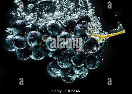 Bunch of red grapes splashing into clear water isolated against black background. Food splash photography Stock Photo