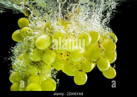 Bunch of white grapes splashing into clear water isolated against black background. Food splash photography Stock Photo