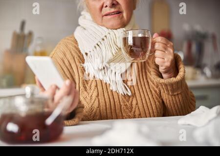 Sick senior woman looking at her phone and staying home Stock Photo