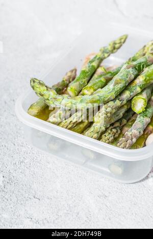 frozen green asparagus pods in a clear white container. on texture. light background. copyspace Stock Photo