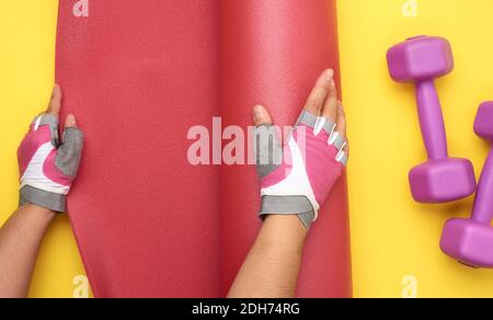 Female hands in sports gloves unfold a red sports mat on a yellow background Stock Photo