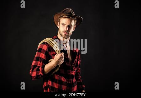 Western life. Lassoing on prairie. Man unshaven cowboy black background. Cowboy wearing hat hold rope. Lasso tool of American cowboy. Still used on ranches to capture cattle or other livestock. Stock Photo